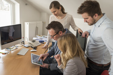 Vier Kollegen im Büro teilen sich ein digitales Tablet - PAF001600