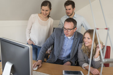 Four colleagues in office looking at computer monitor - PAF001601