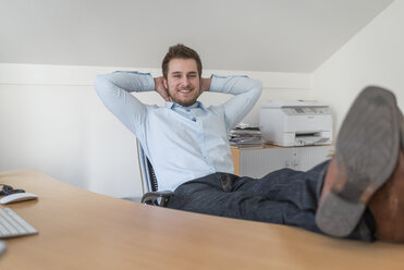 Lächelnder junger Mann im Büro mit Füßen auf dem Schreibtisch - PAF001603