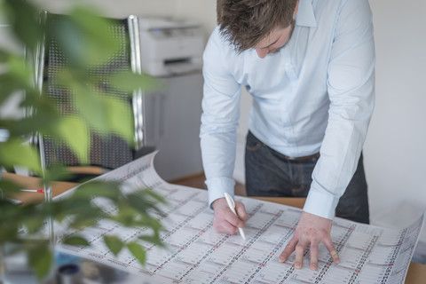 Junger Mann im Büro mit Blick auf den Kalender, lizenzfreies Stockfoto