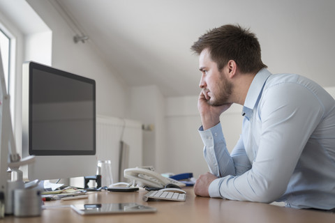 Junger Mann am Schreibtisch im Büro schaut auf den Computerbildschirm, lizenzfreies Stockfoto