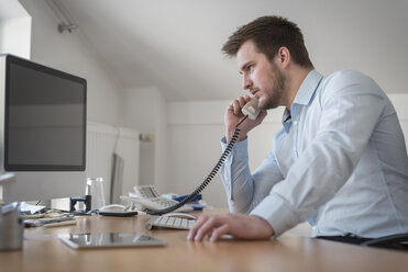 Junger Mann am Schreibtisch im Büro beim Telefonieren - PAF001610