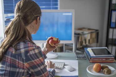 Junge Frau am Schreibtisch im Büro isst einen Apfel - PAF001620