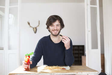 Porträt eines lächelnden jungen Mannes, der Pommes frites mit Ketchup isst - FMKF002476