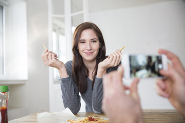 Junger Mann fotografiert seine lächelnde Freundin mit Pommes frites - FMKF002479