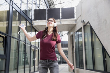 Portrait of young woman listening music with smartphone and headphones - FMKF002486