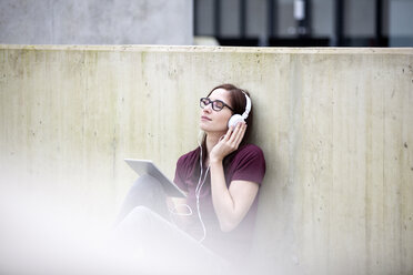 Portrait of young woman listening music with digital tablet and headphones - FMKF002489