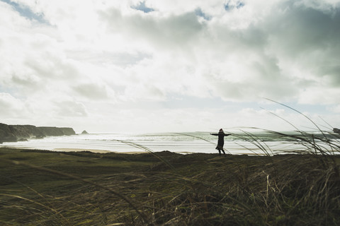 Frankreich, Bretagne, Finistere, Halbinsel Crozon, Frau an der Küste stehend mit ausgestreckten Armen, lizenzfreies Stockfoto