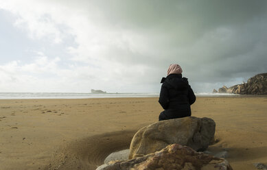 France, Bretagne, Finistere, Crozon peninsula, woman sitting on boulder on the beach - UUF006701