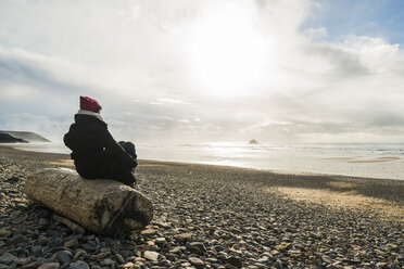 France, Bretagne, Finistere, Crozon peninsula, woman sitting on log on the beach - UUF006714