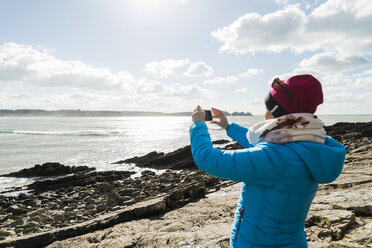 Frankreich, Bretagne, Finistere, Halbinsel Crozon, Frau steht an felsiger Küste und fotografiert - UUF006718