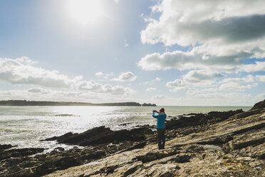 Frankreich, Bretagne, Finistere, Halbinsel Crozon, Frau steht an felsiger Küste und fotografiert - UUF006719