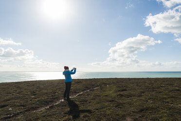 Frankreich, Bretagne, Finistere, Halbinsel Crozon, Frau steht an der Küste und fotografiert - UUF006720