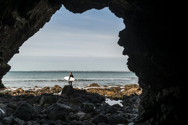 Frankreich, Bretagne, Finistere, Halbinsel Crozon, Mann am felsigen Strand mit Surfbrett - UUF006727