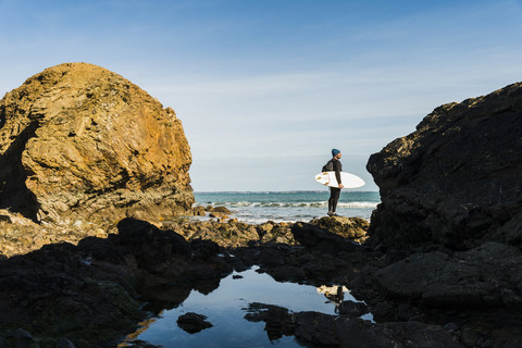 Frankreich, Bretagne, Finistere, Halbinsel Crozon, Mann am felsigen Strand mit Surfbrett, lizenzfreies Stockfoto
