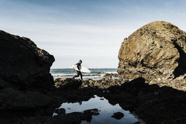 Frankreich, Bretagne, Finistere, Halbinsel Crozon, Mann auf felsigem Strand mit Surfbrett - UUF006729