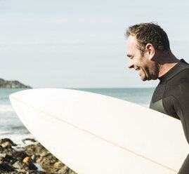 Frankreich, Bretagne, Finistere, Halbinsel Crozon, glücklicher Mann am Strand mit Surfbrett - UUF006730