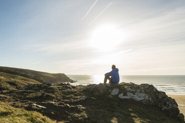Frankreich, Bretagne, Finistere, Halbinsel Crozon, Mann sitzt auf einem Felsen an der Küste - UUF006741