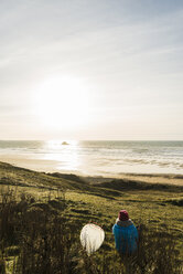 Frankreich, Bretagne, Finistere, Halbinsel Crozon, Frau an der Küste sitzend bei Sonnenuntergang mit Surfbrett - UUF006743