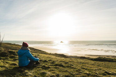 Frankreich, Bretagne, Finistere, Halbinsel Crozon, Frau sitzt bei Sonnenuntergang an der Küste - UUF006745