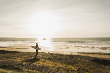 Frankreich, Bretagne, Finistere, Halbinsel Crozon, Mann an der Küste stehend bei Sonnenuntergang mit Surfbrett - UUF006746