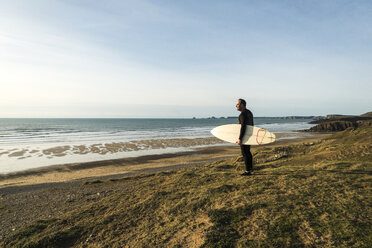 Frankreich, Bretagne, Finistere, Halbinsel Crozon, Mann steht mit Surfbrett an der Küste - UUF006748