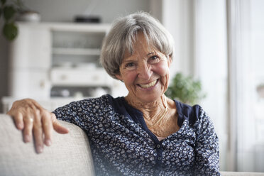 Porträt einer glücklichen älteren Frau, die zu Hause auf der Couch sitzt - RBF004106