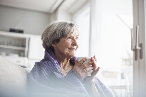 Porträt einer glücklichen älteren Frau, die zu Hause auf der Couch sitzt und eine Tasse Kaffee trinkt, lizenzfreies Stockfoto