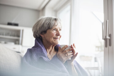Porträt einer glücklichen älteren Frau, die zu Hause auf der Couch sitzt und eine Tasse Kaffee trinkt - RBF004112