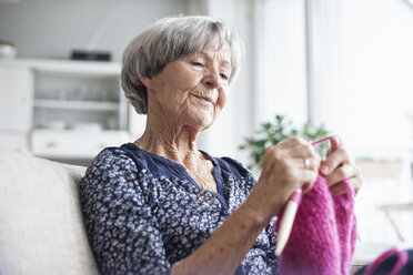 Porträt einer strickenden älteren Frau, die zu Hause auf der Couch sitzt - RBF004113