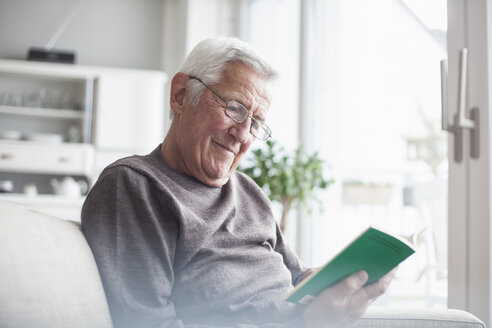 Porträt eines älteren Mannes, der zu Hause auf der Couch sitzt und ein Buch liest - RBF004116