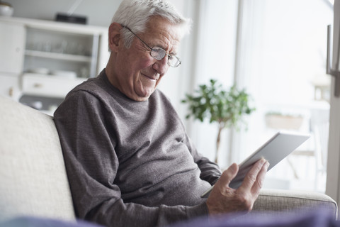Porträt eines älteren Mannes, der zu Hause auf der Couch sitzt und ein digitales Tablet benutzt, lizenzfreies Stockfoto
