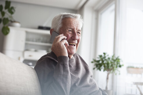 Porträt eines lachenden älteren Mannes, der zu Hause mit seinem Smartphone telefoniert - RBF004119