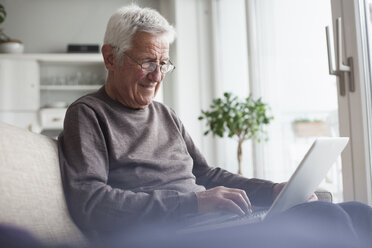 Portrait of senior man sitting on couch at home using laptop - RBF004120
