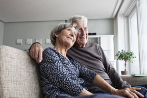 Glückliches älteres Paar sitzt zusammen auf der Couch im Wohnzimmer - RBF004126