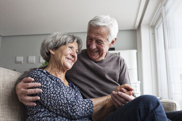 Happy senior couple sitting together on the couch at living room - RBF004130