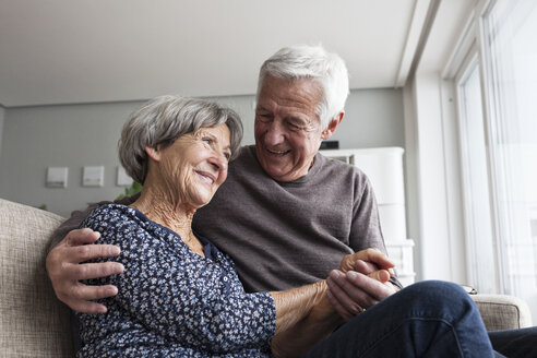 Glückliches älteres Paar sitzt zusammen auf der Couch im Wohnzimmer - RBF004130