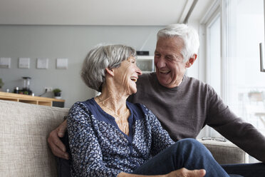 Lachendes älteres Ehepaar, das zusammen auf der Couch im Wohnzimmer sitzt - RBF004131