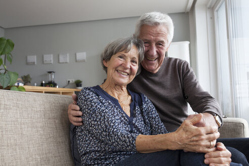 Happy senior couple sitting on the couch in the living room holding hands - RBF004132