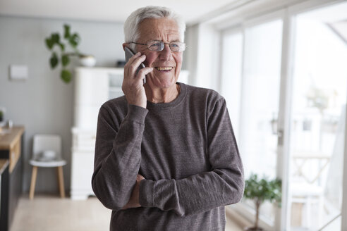 Porträt eines lächelnden älteren Mannes, der zu Hause mit seinem Smartphone telefoniert - RBF004143