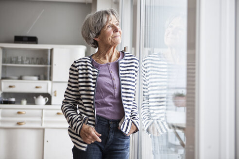 Porträt einer älteren Frau, die durch das Fenster ihres Hauses schaut - RBF004145