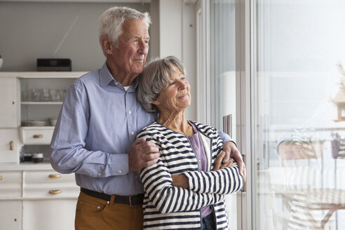 Porträt eines selbstbewussten älteren Paares, das durch das Fenster seines Hauses schaut - RBF004147