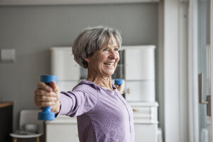 Porträt einer glücklichen älteren Frau bei einer Fitnessübung mit Hanteln zu Hause - RBF004152