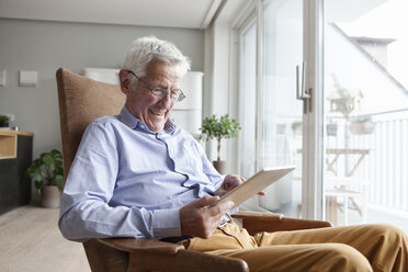 Porträt eines glücklichen älteren Mannes, der zu Hause auf einem Sessel sitzt und ein digitales Tablet benutzt - RBF004157