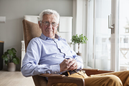 Porträt eines lächelnden älteren Mannes, der zu Hause auf einem Sessel sitzt - RBF004159