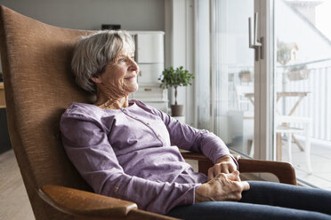 Porträt einer älteren Frau, die zu Hause auf einem Sessel sitzt und durch das Fenster schaut - RBF004169