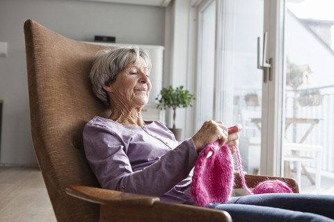 Porträt einer älteren Frau, die zu Hause auf einem Sessel sitzt und strickt, lizenzfreies Stockfoto