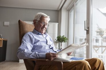 Portrait of senior man sitting on armchair at home reading newspaper - RBF004172