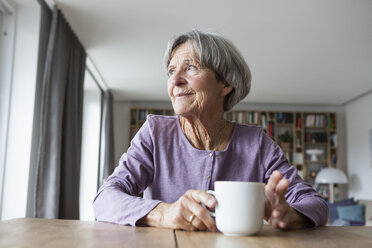 Porträt einer älteren Frau, die mit einer Tasse Kaffee am Tisch sitzt und durch das Fenster schaut - RBF004174