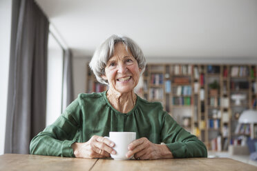 Porträt einer lächelnden älteren Frau, die am Tisch sitzt und eine Tasse Kaffee trinkt - RBF004178
